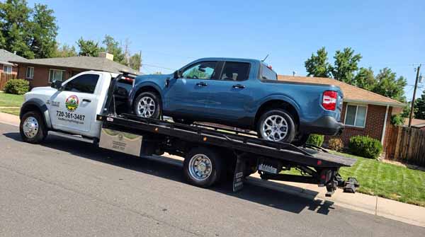 Blue 2024 Ford Maverick on an Auto Recycling Mile High flatbed tow truck during a cash-for-cars pickup in Aurora, Colorado