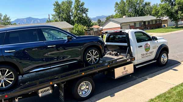 Dark blue 2024 Infiniti QX60 on an Auto Recycling Mile High flatbed tow truck during a cash-for-cars pickup in Denver County, Colorado