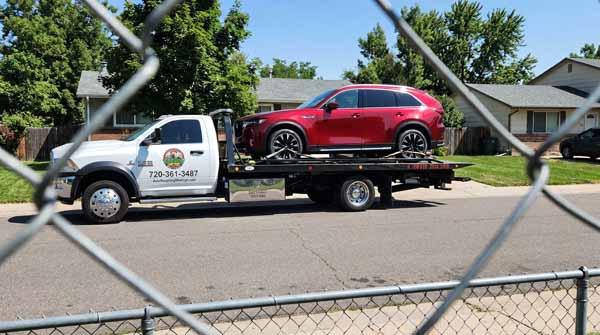 Red 2024 Mazda CX-90 on an Auto Recycling Mile High flatbed tow truck during a cash-for-cars pickup in Greenwood Village, Colorado