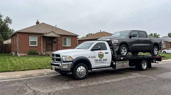 Dark gray 2024 Ram 1500 on an Auto Recycling Mile High flatbed tow truck during a cash-for-cars pickup in Denver, Colorado