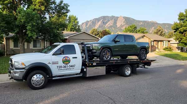 Forest green 2024 Rivian R1T on an Auto Recycling Mile High flatbed tow truck during a cash-for-cars pickup in Denver, Colorado