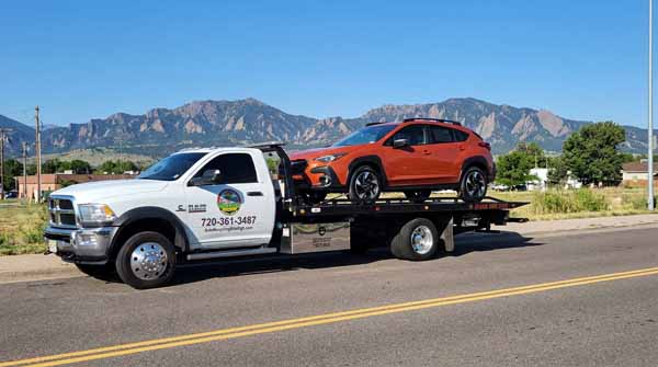 Orange 2024 Subaru Crosstrek on an Auto Recycling Mile High flatbed tow truck during a cash-for-cars pickup in Aurora, Colorado