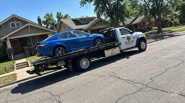 Blue 2024 Toyota Camry on an Auto Recycling Mile High flatbed tow truck during a cash-for-cars pickup in Denver, Colorado