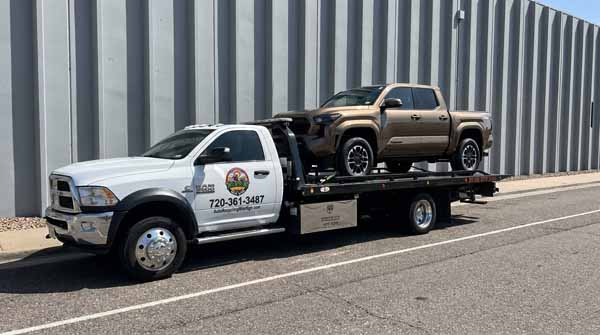 Bronze 2024 Toyota Tacoma on an Auto Recycling Mile High flatbed tow truck during a cash-for-cars pickup in Arvada, Colorado