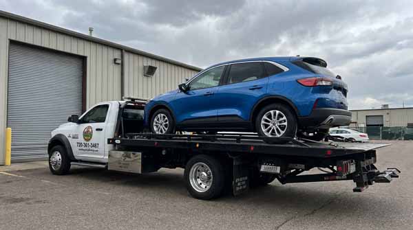 Blue 2025 Ford Escape on an Auto Recycling Mile High flatbed tow truck during a cash-for-cars pickup in Denver County, Colorado