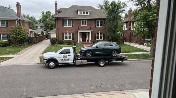Dark green 2025 Genesis GV70 on an Auto Recycling Mile High flatbed tow truck during a cash-for-cars pickup in Denver County, Colorado