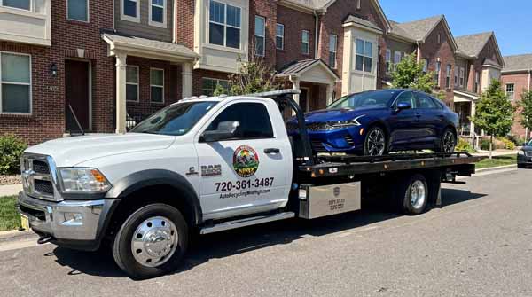 Dark blue 2025 Kia K5 on an Auto Recycling Mile High flatbed tow truck during a cash-for-cars pickup in Lakewood, Colorado