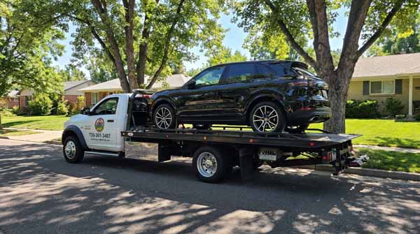 Black 2025 Porsche Cayenne on an Auto Recycling Mile High flatbed tow truck during a cash-for-cars pickup in Denver, Colorado