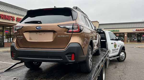 Bronze 2025 Subaru Outback on an Auto Recycling Mile High flatbed tow truck during a cash-for-cars pickup in Thornton, Colorado