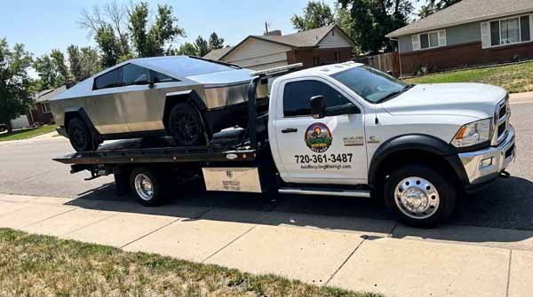 Stainless steel 2025 Tesla Cybertruck on an Auto Recycling Mile High flatbed tow truck during a cash-for-cars pickup in Denver, Colorado
