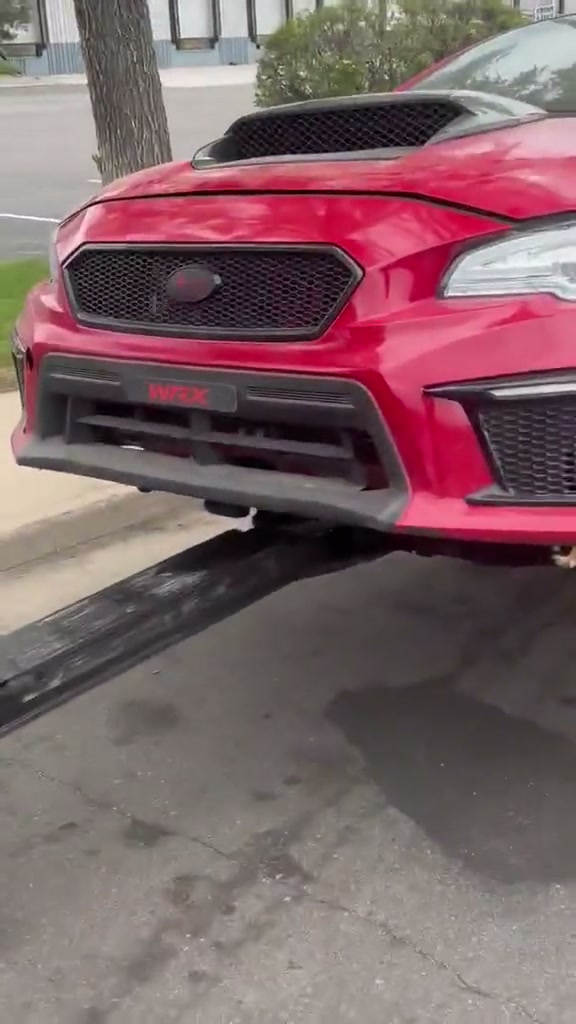 Rear view of a red Subaru WRX STI with a large wing on tow dollies behind an Auto Recycling Mile High black wrecker